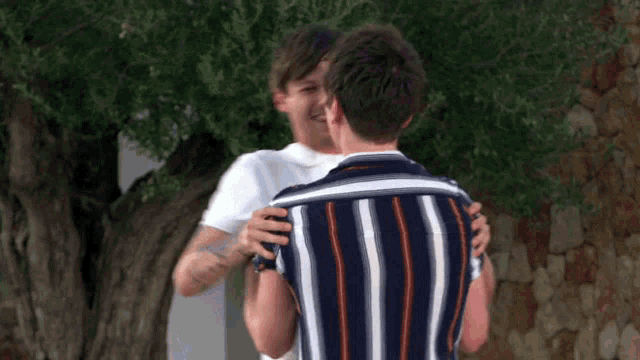 two men hugging each other in front of a stone wall