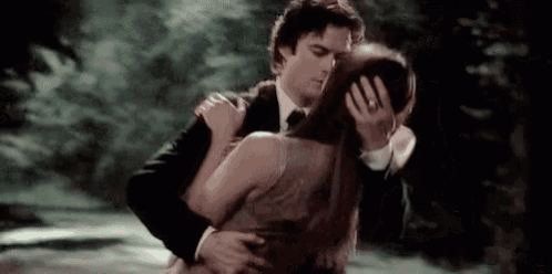 a man in a suit and tie is hugging a woman in a dress and kissing her on the forehead .