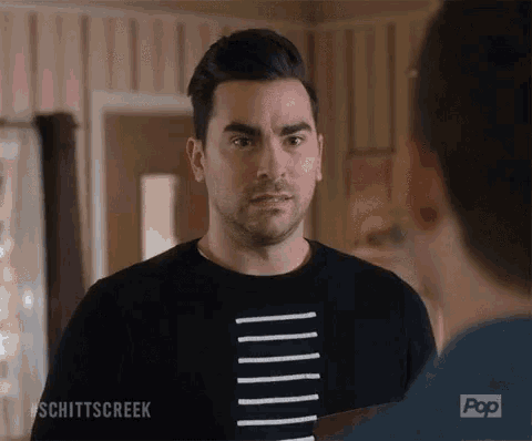 a man in a black striped shirt is looking at another man in a room .