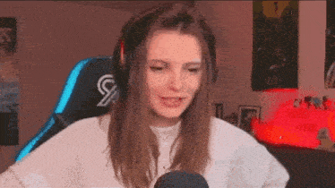 a woman wearing headphones and a white sweater is sitting in a gaming chair .
