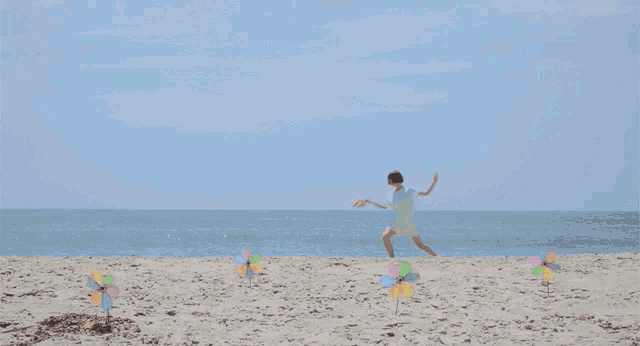 a woman in a white dress is running on a beach with windmills