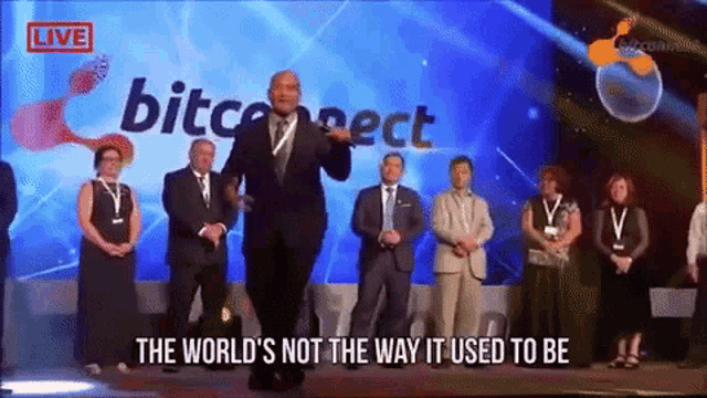 a man stands on a stage in front of a screen that says bitconnect