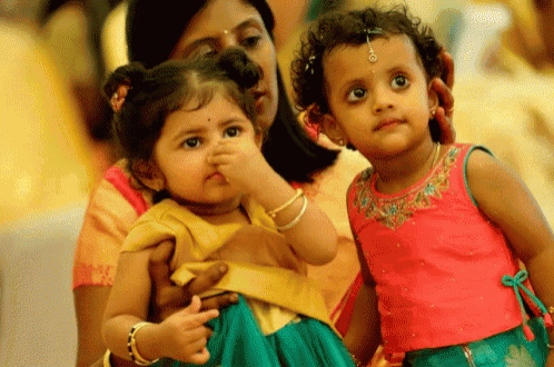 two little girls are standing next to each other and one is covering her nose with her hand