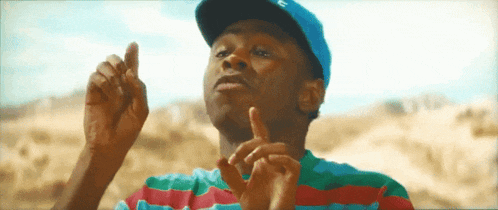 a man wearing a hat and a striped shirt is making a peace sign .