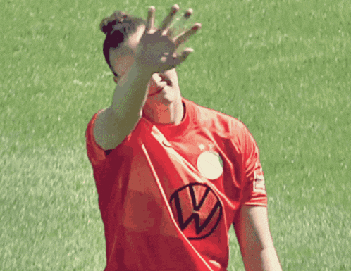 a person wearing a red shirt with a vw logo on it covering their face