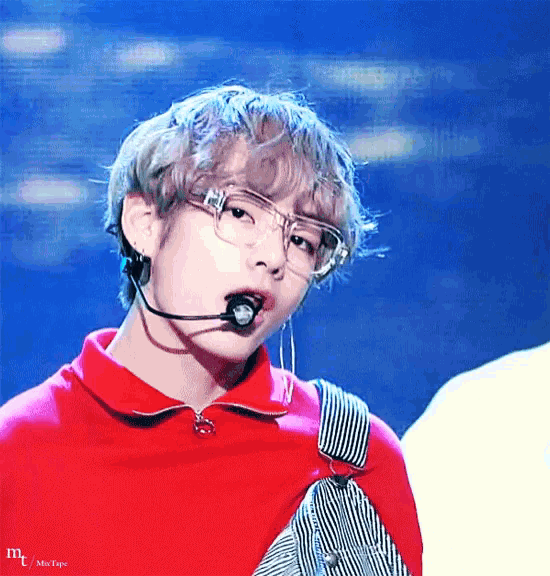 a close up of a person wearing glasses and a red shirt with a microphone in their mouth