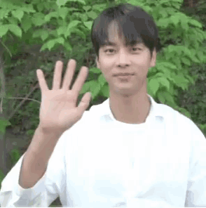 a young man in a white shirt is waving at the camera .