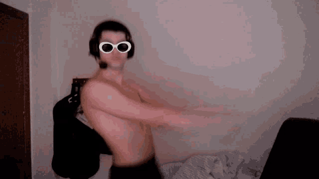 a shirtless man wearing headphones and goggles stands in a room