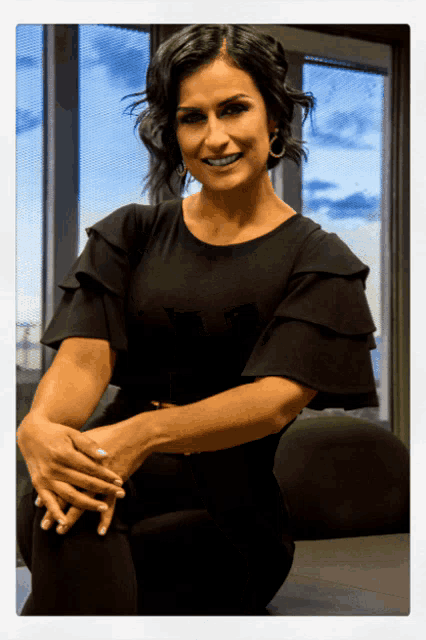 a woman in a black dress sits with her hands folded