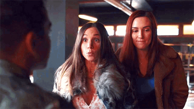 two women are standing next to each other talking to a man .
