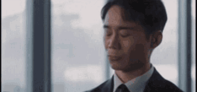 a man in a suit and tie is sitting in front of a window .