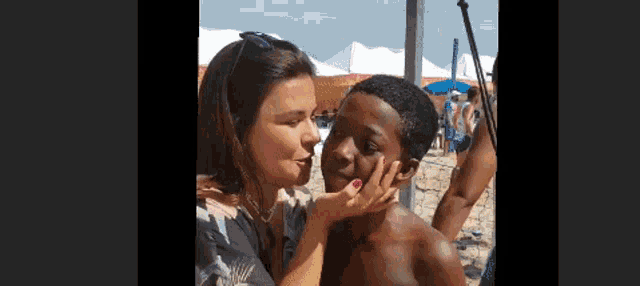 a woman is touching a boy 's face on a beach