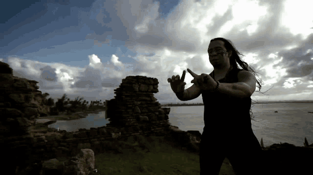a man in a black tank top is standing in front of a body of water and giving the middle finger