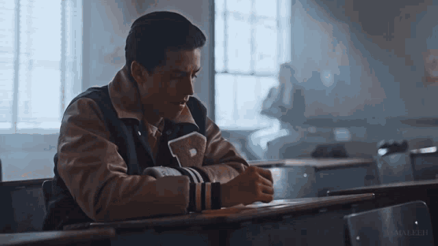 a man wearing a varsity jacket with the letter p on it sits at a desk