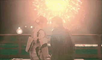 a man and woman are sitting on a bench watching fireworks .