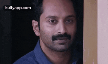 a man with a beard and mustache is standing next to a wall and looking at the camera .