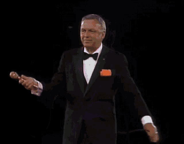 a man in a tuxedo is holding a microphone in his hand