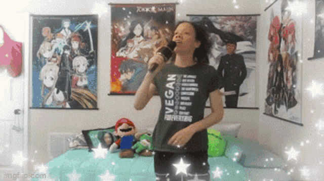a girl is singing into a microphone in a room with posters on the wall