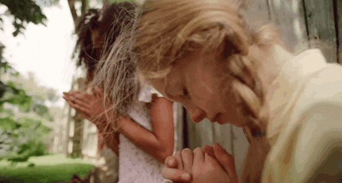 two young girls are praying together with their hands folded in front of a wooden wall .
