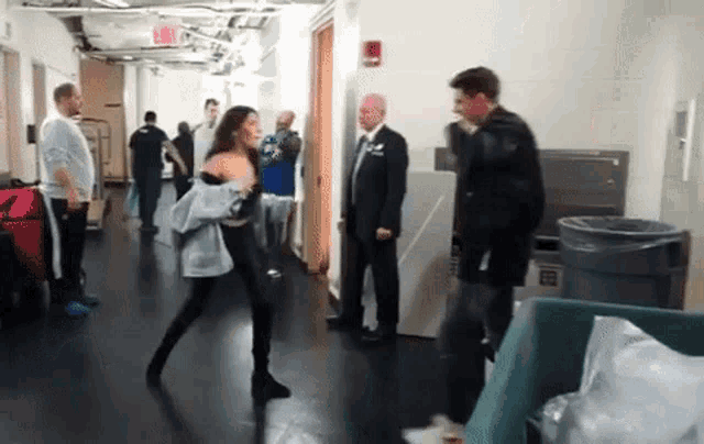 a woman is dancing in a hallway while a man in a suit looks on .