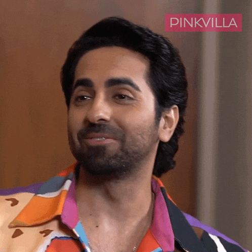 a man with a beard wearing a colorful shirt with pinkvilla written on the bottom