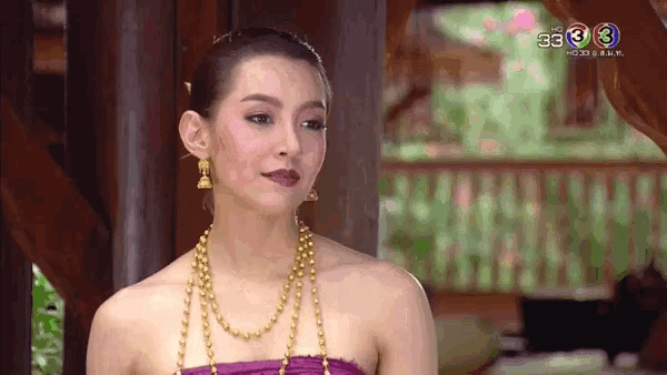 a woman wearing a purple dress and a gold necklace is standing in front of a window .