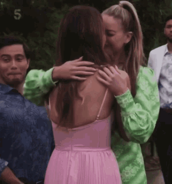 a woman in a pink dress is hugging a woman in a green dress