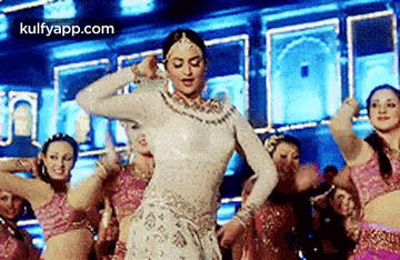 a woman in a white dress is dancing in front of a group of women in pink dresses .