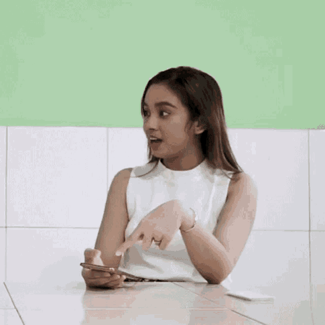 a woman is sitting at a table with her hands in the air while holding a cell phone .