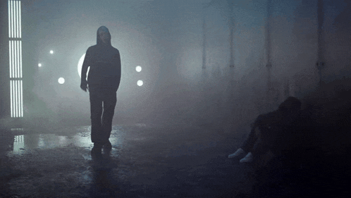 a man in a hooded jacket stands in a foggy room