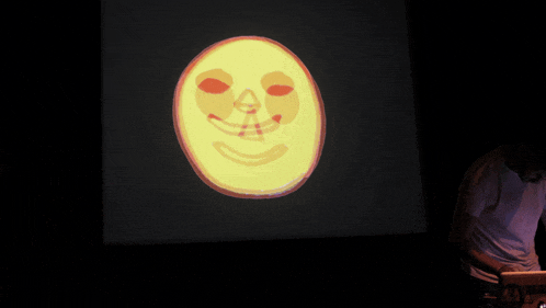 a man stands in front of a projection of a yellow face