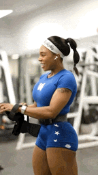 a woman in a blue shirt and blue shorts is smiling in a gym .