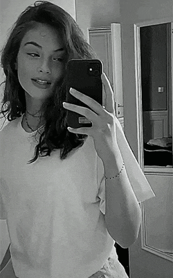 a black and white photo of a woman taking a selfie in front of a mirror .