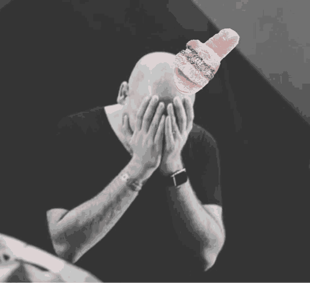 a bald man covering his face with his hands and a pair of pink slippers on top of his head