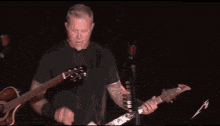 a man in a black shirt is playing a guitar on a stage