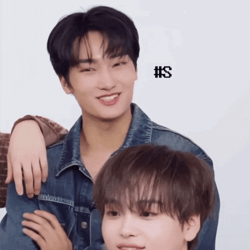 a man in a denim jacket stands next to another man with #s on the bottom right