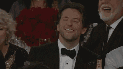 a man in a tuxedo and bow tie is smiling while sitting in a crowd of people .