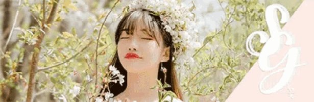 a woman wearing a wreath of white flowers on her head is standing in front of a tree with her eyes closed .