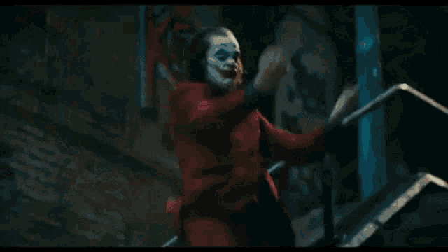 the joker is walking down the stairs in a red suit .