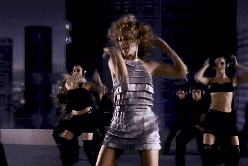 a woman in a silver dress is dancing in front of a crowd of dancers