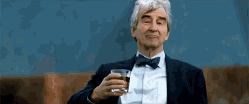 a man in a tuxedo and bow tie holds a glass of whiskey