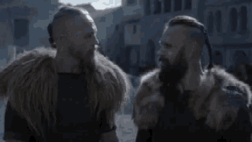 two men with beards and fur coats are standing next to each other in a city street .