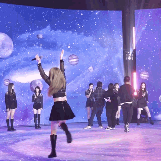 a woman in a black skirt is holding a microphone in front of a large screen