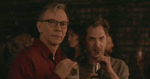 two men sitting at a table drinking through straws