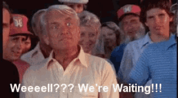 an older man is standing in front of a crowd of people and says weeeeell ? we 're waiting !!!