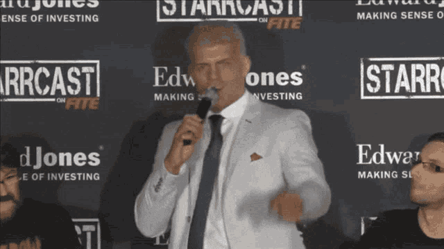 a man in a suit and tie is speaking into a microphone in front of a wall that says starcast on fite