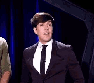 a man in a suit and tie is standing in front of a blue curtain and making a funny face .