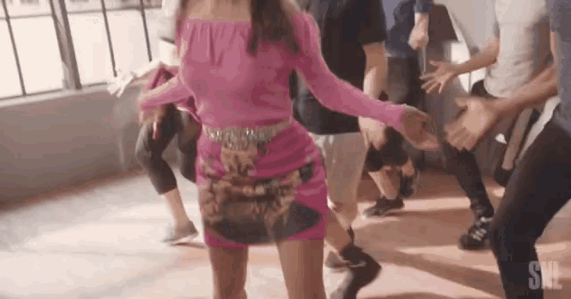 a woman in a pink dress is dancing in front of a group of people .