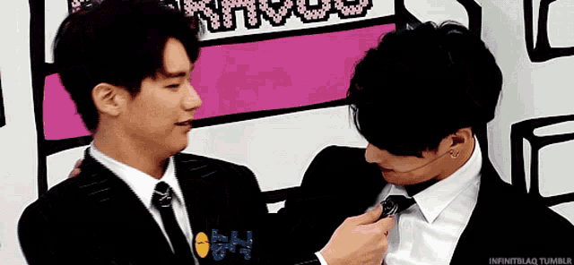 two men in suits are standing next to each other and one of them is fixing another man 's tie ..