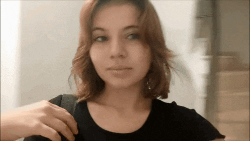 a woman with short red hair is wearing a black shirt and holding a black bag .